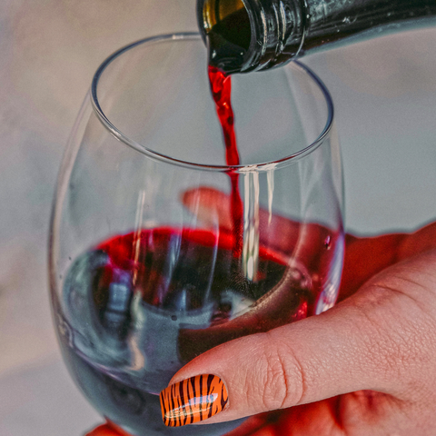 Women with jazzy tiger stripped fingernails cradling a glass of deep red wine whilst being poured 