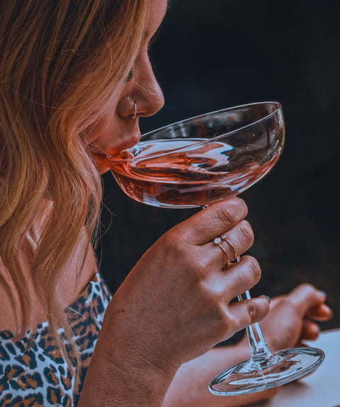 A sophisticated women drinking a dark and vibrant coloured rose wine from a coupe glass